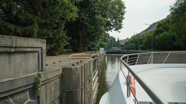 An excursion boat enters the historic Smichov canal lock in Prague on the Vltava River. This waterway sluice gate enables urban river navigation. Ideal for European travel and river cruising.