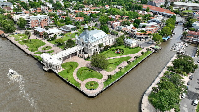 Aerial view of Museo de Arte de Tigre situated on a riverbank with manicured gardens, a white colonnade, and a small boat moving through the water in Tigre, Provincia de Buenos Aires, Argentina.