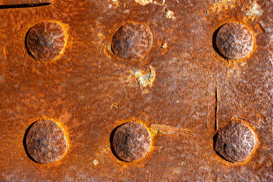 Close up of rusty metal plate with old rivets, showing corrosion, oxidation and weathered industrial texture for engineering, construction, maintenance, aging infrastructure and decay concepts.
