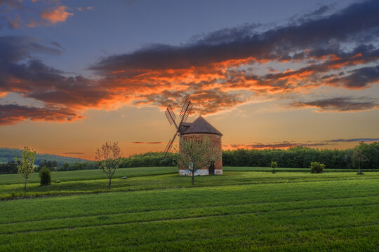 Aerial view of the historic windmill surrounded by lush green fields and trees under a vibrant sunset sky in Kunkovice, Zlin Region, Czechia.