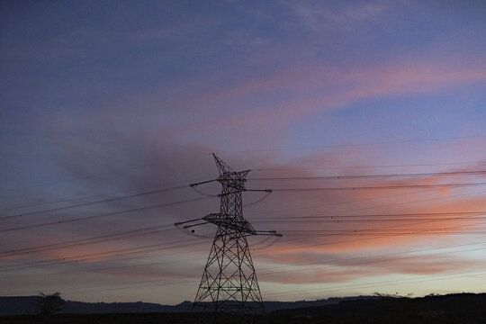 View of Kenya Power Suswa Substation with a tall transmission tower silhouetted against a vibrant sunset sky in Mirera, Nakuru County, Kenya.