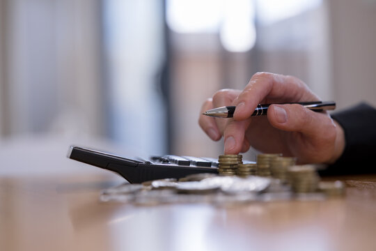 Hand using calculator with stacked coins for financial planning and budgeting, representing savings, investment, money management, accounting, expenses, personal finance and wealth growth strategy.