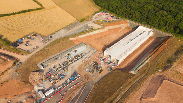 Aerial view of the HS2 railway construction site with a concrete tunnel portal, heavy machinery, and excavation works surrounded by fields in Long Itchington, England, United Kingdom.