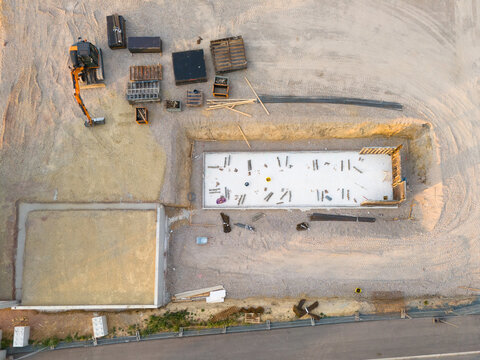 Aerial view of a construction site with a concrete foundation, wooden formwork, an excavator, and building materials on gravel ground in Trier-Saarburg, Rhineland-Palatinate, Germany.