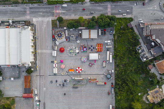 Aerial view of a traveling carnival with colorful rides, tents, and trucks set up in a large parking lot in Avellino, Campania, Italy.