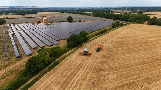 Aerial view of solar farm construction adjacent to a harvested field with a tractor in Great Wymondley, England, United Kingdom.