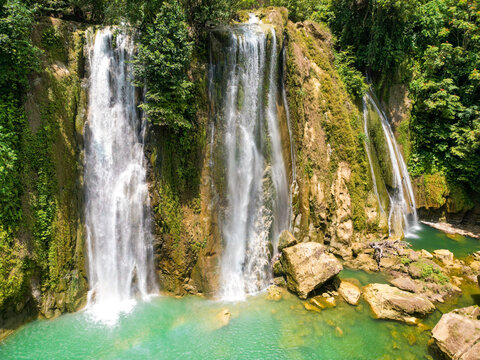 Aerial view of Cikaso Waterfall with three cascading streams falling into a turquoise pool surrounded by lush green tropical vegetation and rocky cliffs in Kramatmulya, West Java, Indonesia.