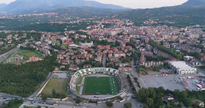 Aerial view of the Stadio Partenio-Adriano Lombardi stadium surrounded by urban buildings and lush green hills in Avellino, Campania, Italy.