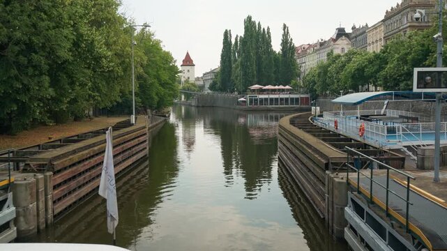 Excursion boat exits Smichov canal lock onto Vltava River in Prague. Waterway tour view displays historic Sitkov Water Tower. Ideal scene for European travel and river cruising vacation.