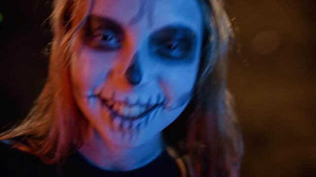 Portrait of Caucasian girl with skeleton face paint rolling eyes and smiling creepily. Perfect for Halloween marketing campaigns, spooky event promos, or horror-themed commercial content