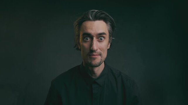 Oh wow, it appeared. Close-up studio portrait of a middle-aged man with gray-streaked hair in a black collared shirt, showcasing various facial expressions against a dark blurred background