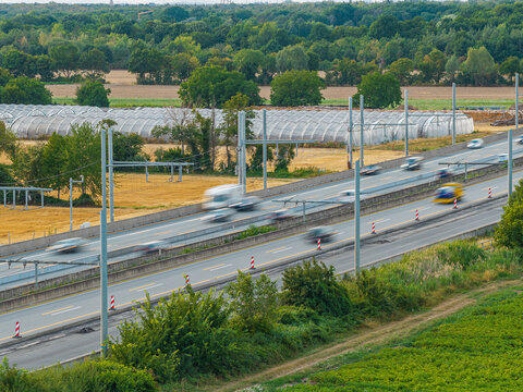 Aerial view of the eHighway test track for electric trucks with overhead power lines, featuring moving vehicles, surrounded by fields and greenhouses in Weiterstadt, Hessen, Germany.