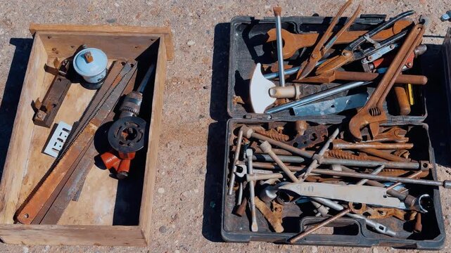 Rusty tools in boxes on asphalt, summer street flea market scene showing assorted vintage hand tools, saw, wrenches, hammers