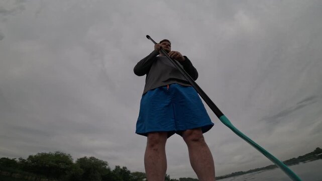 Man paddling SUP on cloudy lake
