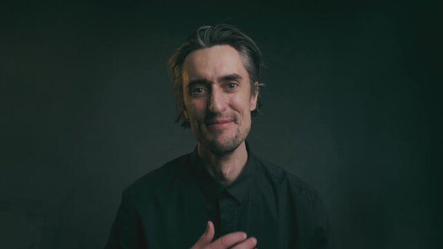 laughter hand at heart soulfully Close-up portrait of an adult man with dark hair and stubble in a black collared shirt, showcasing varied facial expressions against a dark gradient background