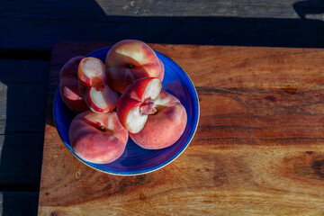 Fresh organic donut peaches, some sliced, resting in a blue bowl on a rustic wooden surface, highlighting healthy eating © JOSEANTONA