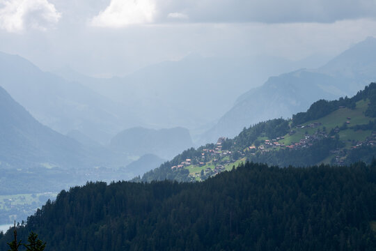 View of the mountainous landscape near Interlaken with a village on the hillside, pine forests in the foreground, and hazy peaks in Interlaken, Canton of Bern, Switzerland.