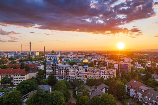 Aerial view of the Waldspirale residential complex with its colorful facade and green roof under a vibrant sunset sky in Darmstadt, Hessen, Germany.