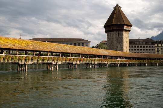 View of the historic Chapel Bridge and Wasserturm adorned with vibrant flowers over the Reuss river in Lucerne, Lucerne, Switzerland.