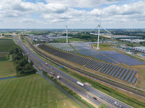 Aerial view of a solar farm and wind turbines situated next to a highway with traffic in the Netherlands.