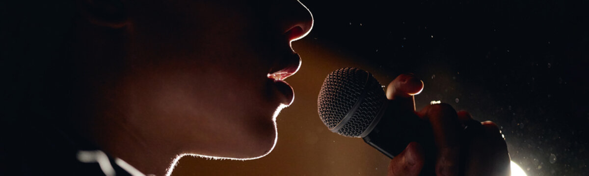 Teenager performing on stage during student theater production holding microphone. Image suitable for promoting youth arts programs, drama education, and talent shows, extreme close up