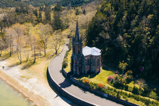 Aerial view of Ermida de Nossa Senhora das Vitorias surrounded by lush forest and the shore of Lagoa das Furnas, Furnas, Acores, Portugal.