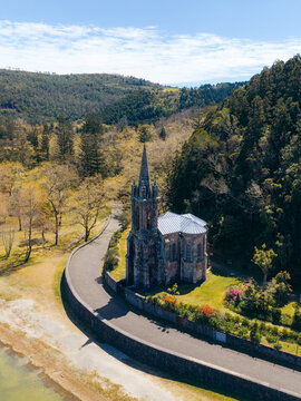 Aerial view of Ermida de Nossa Senhora das Vitorias chapel on the shore of Furnas Lake surrounded by lush forest and green hills in Furnas, Acores, Portugal.