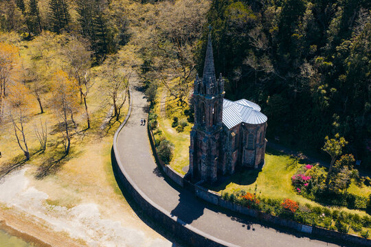 Aerial view of Ermida de Nossa Senhora das Vitorias surrounded by lush trees and a winding path near the lake in Furnas, Acores, Portugal.