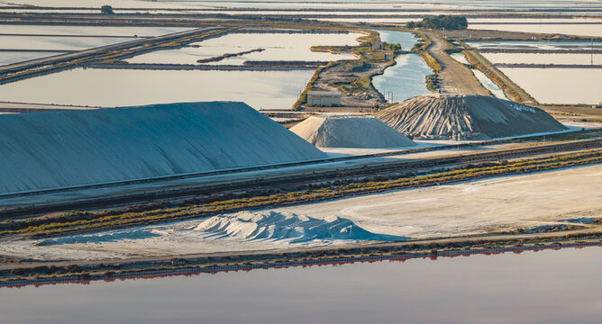 Aerial view of salt storage piles and evaporation ponds in the Camargue region with pink water and textured mounds of harvested sea salt in Aigues-Mortes, Occitanie, France.