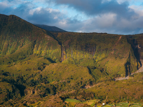 View of Flores Island in the Azores, Portugal, featuring lush green mountains, cascading waterfalls, and agricultural fields under a cloudy sky, Azores, Portugal.