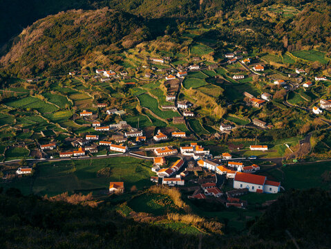 View of Flores Island featuring traditional white houses with orange roofs nestled among lush green terraced fields and rolling hills in Azores, Portugal.