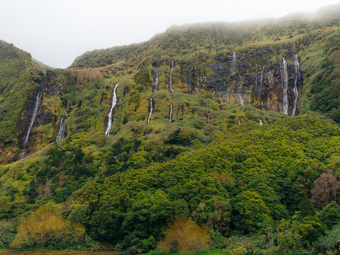 View of the waterfalls cascading down the lush green cliffs of Flores Island, Azores, Portugal.