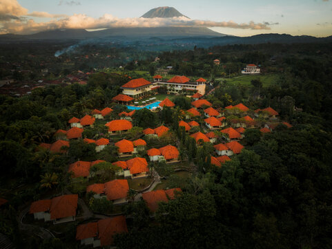 Aerial view of a resort complex with orange-tiled roofs, a swimming pool, and lush tropical gardens set against the backdrop of Mount Agung in Kecamatan Karangasem, Bali, Indonesia.