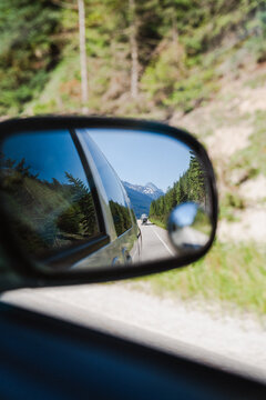 View of the reflection of a mountain road and coniferous forest in a car side mirror in Squamish, British Columbia, Canada.