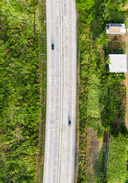 Aerial view of a straight concrete highway surrounded by lush green vegetation and small buildings in Malang, East Java, Indonesia.