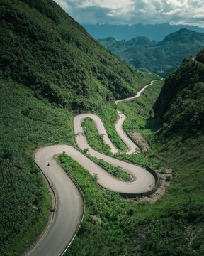 Aerial view of the winding Ha Giang Loop mountain road surrounded by lush green slopes and dramatic mountain peaks in Ha Giang, Ha Giang, Vietnam.