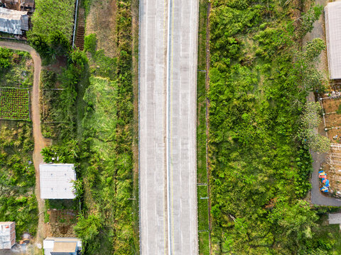 Aerial view of an Indonesian toll road cutting through lush green vegetation and agricultural fields in Malang, East Java, Indonesia.