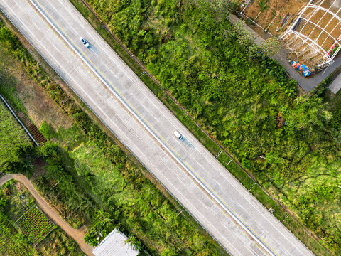 Aerial view of an Indonesian toll road with cars driving along the concrete highway surrounded by lush green vegetation and rural landscape in Malang, East Java, Indonesia.