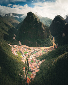 Aerial view of the town of Aguas Calientes nestled in a deep valley surrounded by lush green mountains and the Urubamba River in Aguas Calientes, Cusco, Peru.