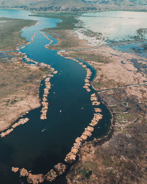 Aerial view of the Uros floating islands on Lake Titicaca with traditional reed structures and boats in the dark blue water surrounded by marshy landscape in Puno, Puno, Peru.