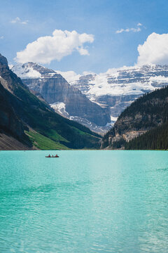 View of Lake Louise with a canoe carrying people on the turquoise water, framed by snow-capped mountains and pine forests in Lake Louise, Alberta, Canada.