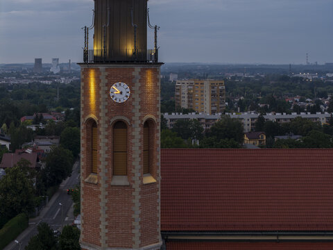 Aerial view of the Church of Our Lady of Good Counsel in Prokocim with its illuminated clock tower and red roof at dusk in Krakow, Malopolskie, Poland.