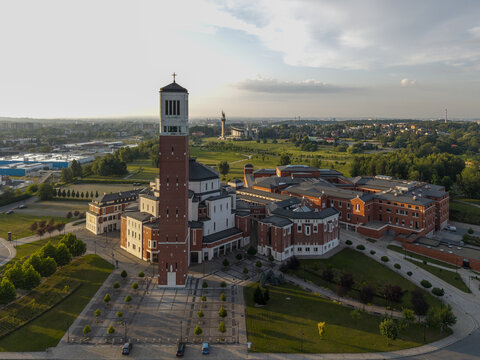 Aerial view of The Centre of John Paul II Pontificate featuring a tall red brick bell tower and modern complex surrounded by green lawns in Krakow, Malopolskie, Poland.