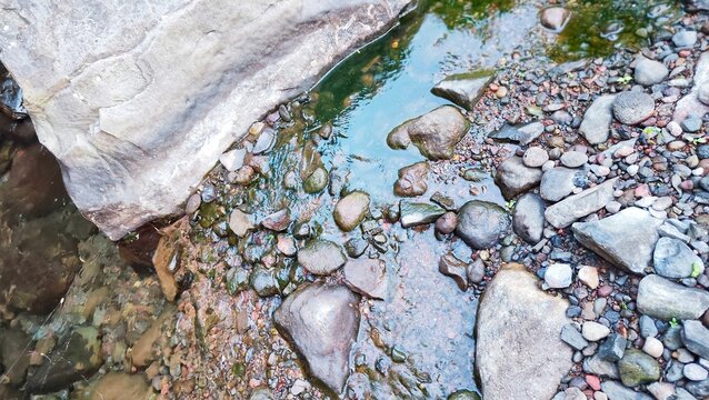 The flow of water creates green reflections on dark river stones