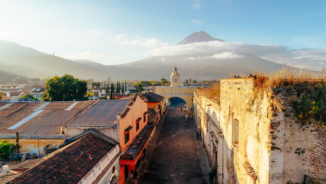 Aerial view of Santa Catalina Arch with Volcan de Agua in the background, featuring historic colonial architecture and cobblestone streets in Antigua Guatemala, Sacatepequez, Guatemala.