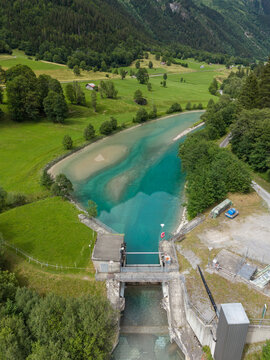 Aerial view of a concrete water intake structure and turquoise reservoir in the lush green alpine valley of Gadmen, Switzerland.
