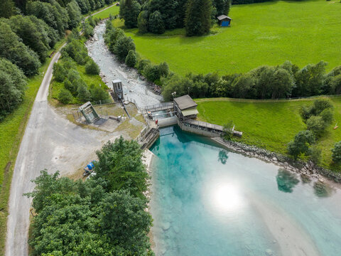 Aerial view of an alpine water reservoir and concrete dam infrastructure surrounded by lush green meadows and forests in Gadmen, Switzerland.