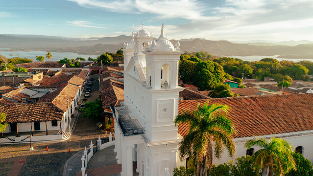 Aerial view of the white Santa Lucia Church in Suchitoto, featuring red tile roofs, palm trees, and Suchitlan Lake at golden hour in Suchitoto, Cuscatlan Department, El Salvador.