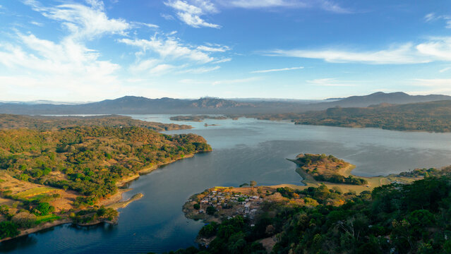 Aerial view of Lake Suchitlan with its surrounding lush green hills and a small settlement on the shore in Suchitoto, Cuscatlan Department, El Salvador.
