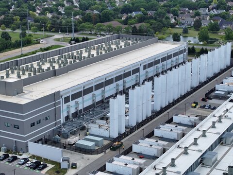 Aerial view of a large data center facility featuring extensive cooling units, HVAC systems, and a parking lot set within a suburban landscape in the United States.